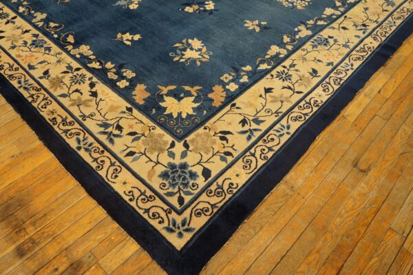 Deep blue rug with scattered florals and a wide beige, blue-patterned border on wood flooring.