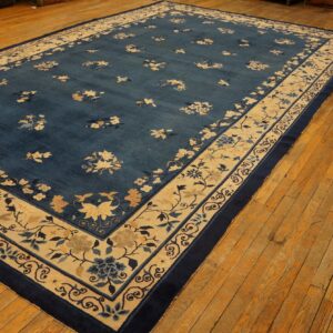 Deep blue floral rug with a wide tan and navy border resting on wide plank wood flooring.