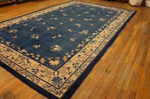 Deep blue floral rug with a wide tan and navy border resting on wide plank wood flooring.