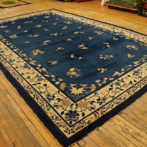 Large navy floral rug with a wide beige border lies on distressed wooden floors.