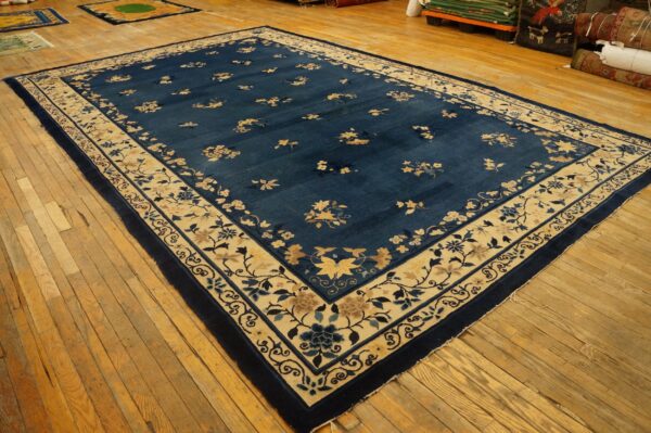 Large navy floral rug with a wide beige border lies on distressed wooden floors.