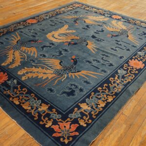 Dark blue rug with tan phoenix motifs and coral flowers sits on light, distressed wooden floorboards.