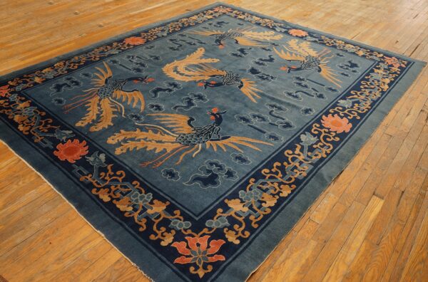 Dark blue rug with tan phoenix motifs and coral flowers sits on light, distressed wooden floorboards.