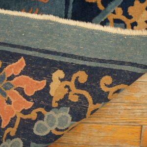 Close-up of a navy blue, salmon, and tan floral rug border folded back on distressed wood floors.