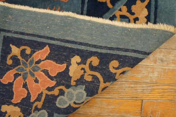 Close-up of a navy blue, salmon, and tan floral rug border folded back on distressed wood floors.