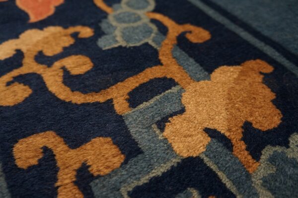 Navy blue rug detail featuring plush pile, golden scrolling motifs, dusty blue, and coral accents.