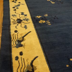 Deep blue rug with yellow border featuring birds and flowers rests on distressed hardwood planks.