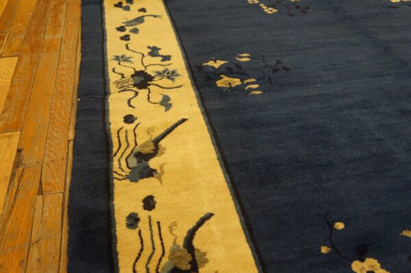 Deep blue rug with yellow border featuring birds and flowers rests on distressed hardwood planks.