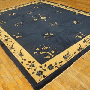 Navy area rug with cream and blue floral and bird motifs rests on golden hardwood floors.