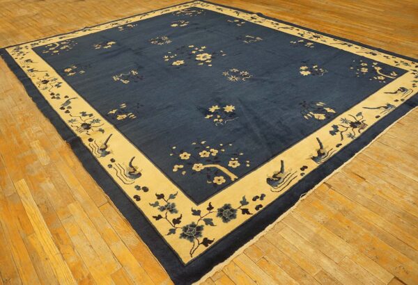 Navy area rug with cream and blue floral and bird motifs rests on golden hardwood floors.