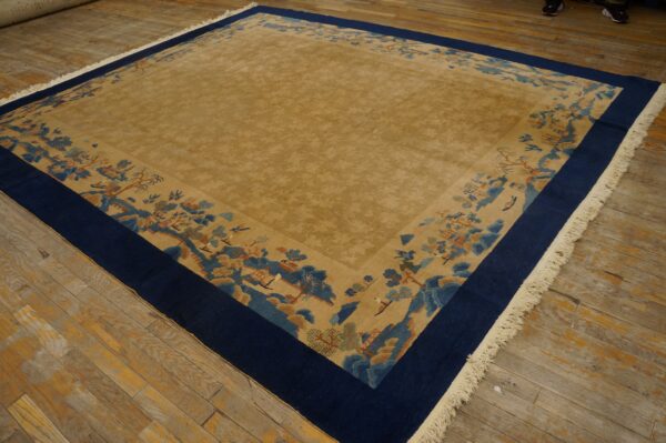 Low pile gold rug with a blue and tan scenic border resting on distressed wood flooring.