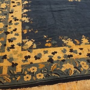 Navy blue rug featuring a bold gold and teal floral border rests on distressed wood flooring.