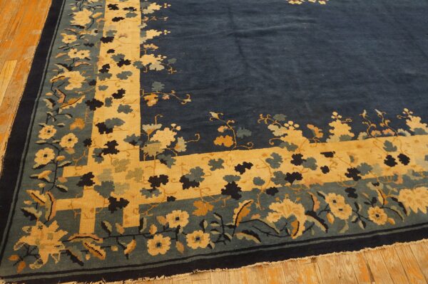 Navy blue rug featuring a bold gold and teal floral border rests on distressed wood flooring.