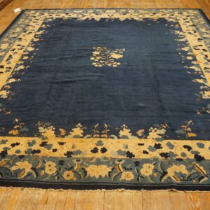Plush navy blue rug with yellow and teal floral borders and a central spray rests on hardwood floors.