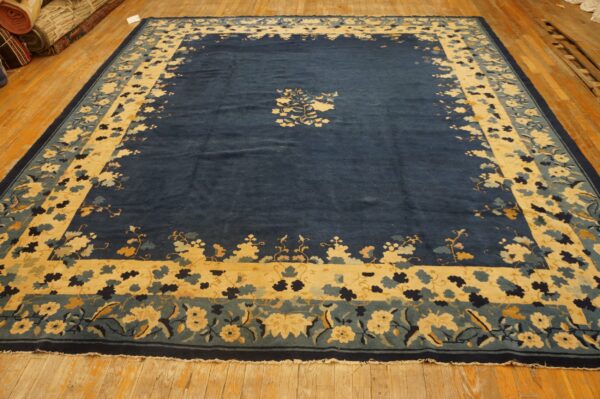 Plush navy blue rug with yellow and teal floral borders and a central spray rests on hardwood floors.