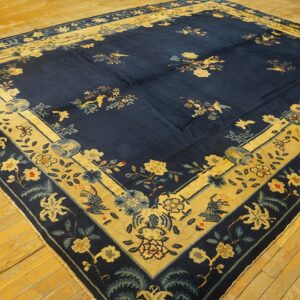 Navy area rug with wide tan and blue floral borders rests on aged yellow hardwood planks.