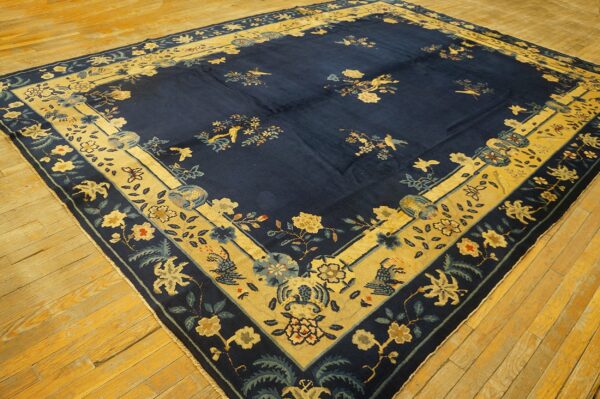 Navy area rug with wide tan and blue floral borders rests on aged yellow hardwood planks.