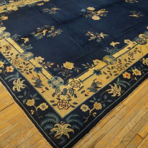Navy blue rug with a yellow-gold border and floral bird motifs rests on distressed hardwood floors.