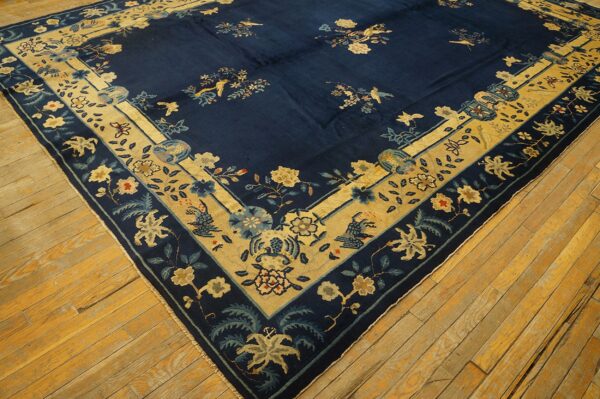 Navy blue rug with a yellow-gold border and floral bird motifs rests on distressed hardwood floors.