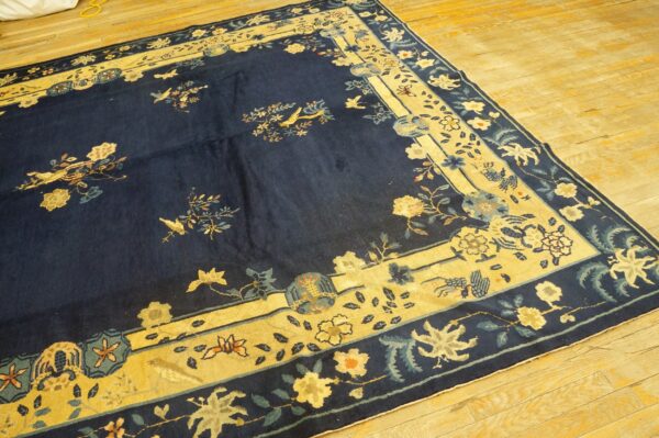 Dark blue rug featuring light yellow borders, florals, and birds, placed over bright wood flooring.