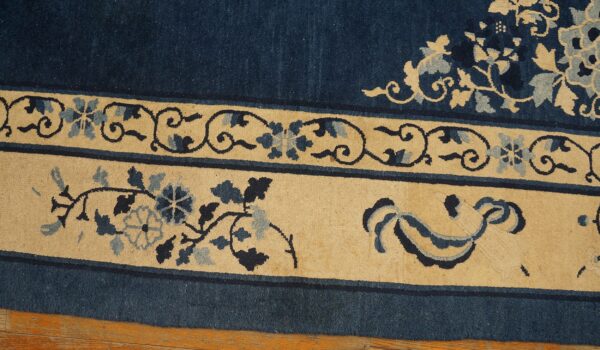 This rug detail highlights the deep blue field bordered by cream panels with intricate floral patterns.