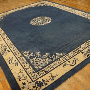 Low-pile indigo rug featuring a large cream floral border and center medallion on worn wood floors.