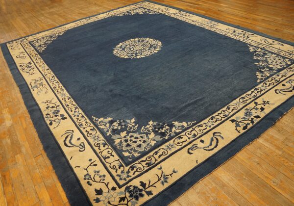 Low-pile indigo rug featuring a large cream floral border and center medallion on worn wood floors.