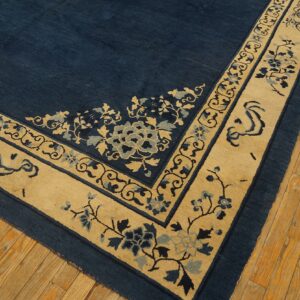 Corner detail of a deep blue rug with a light beige border featuring stylized floral and scroll designs.