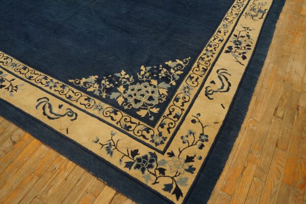 Corner detail of a deep blue rug with a light beige border featuring stylized floral and scroll designs.