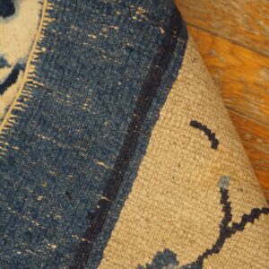 The corner of a blue and beige textured rug with floral patterns is rolled back on wood flooring.