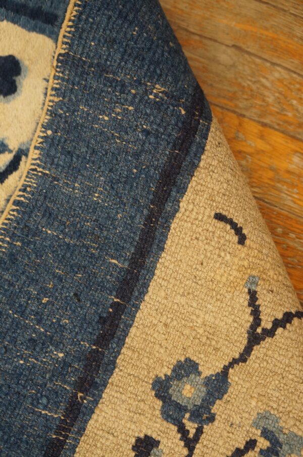 The corner of a blue and beige textured rug with floral patterns is rolled back on wood flooring.