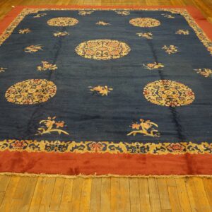 Large navy rug with golden medallions and scattered flowers, framed by a wide terracotta-red border on wood.