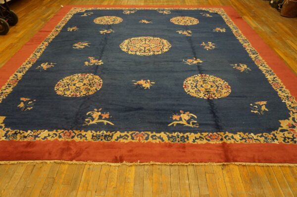 Large navy rug with golden medallions and scattered flowers, framed by a wide terracotta-red border on wood.