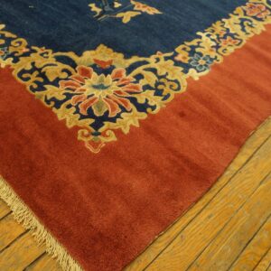 Detail of a blue rug corner with a red border and tan floral motifs, showing fringe on wood planks.