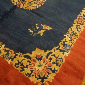 Navy rug with dense gold floral patterns and a wide rust-colored border on hardwood flooring.