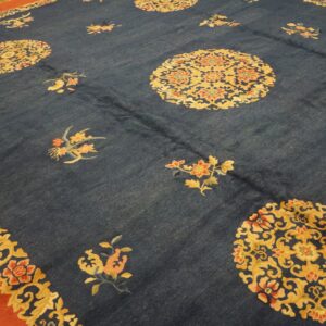 A large navy rug features golden floral medallions, scattered motifs, and a wide rust-colored outer border.