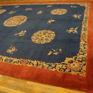 Dark blue rug with gold and coral floral medallions and a wide rust border covers wood plank flooring.
