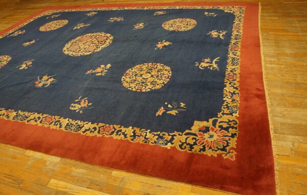 Dark blue rug with gold and coral floral medallions and a wide rust border covers wood plank flooring.