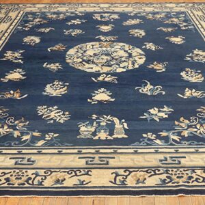 Dark blue rug featuring cream geometric borders and scattered floral motifs rests on wood plank flooring.