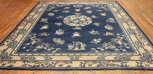 Dark blue rug featuring cream geometric borders and scattered floral motifs rests on wood plank flooring.