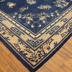 Corner view of a navy blue rug with scattered floral patterns and a wide beige geometric border on wood floors.