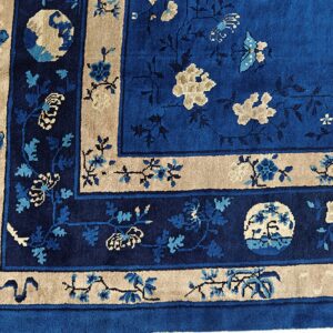 Corner of a deep blue floral rug bordered in tan, showing detailed vines and contrasting medallions.