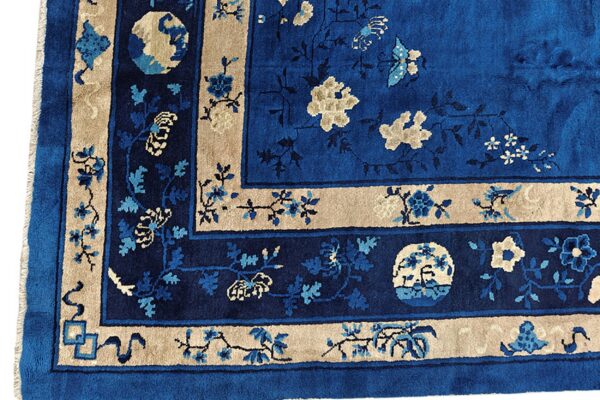 Corner of a deep blue floral rug bordered in tan, showing detailed vines and contrasting medallions.