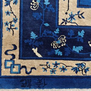 Textured rug corner in deep blue and tan with vine motifs and visible Chinese characters along the edge.