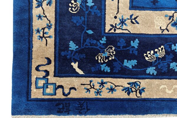 Textured rug corner in deep blue and tan with vine motifs and visible chinese characters along the edge.