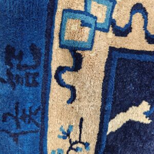 Plush blue and tan rug detail showing geometric border patterns and small light blue flowers.