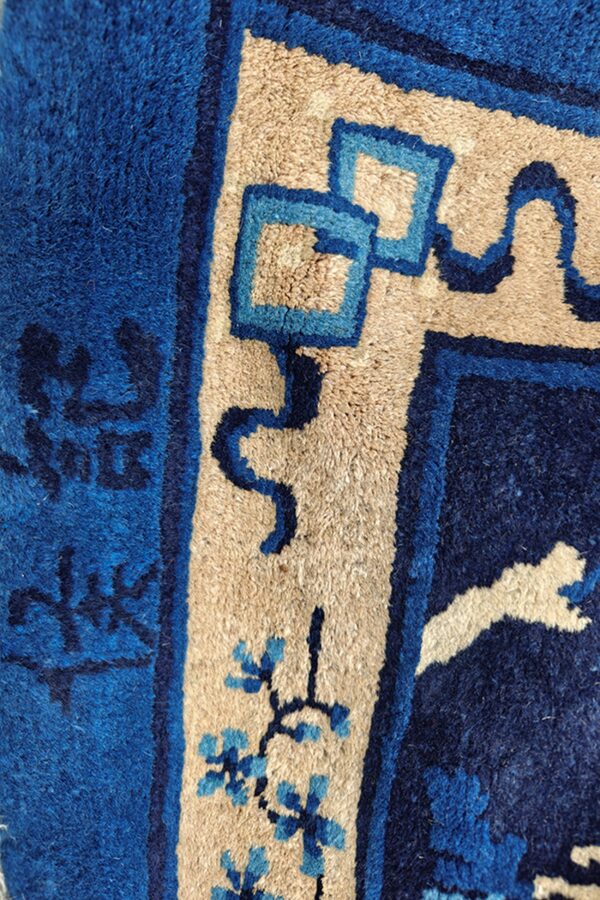 Plush blue and tan rug detail showing geometric border patterns and small light blue flowers.