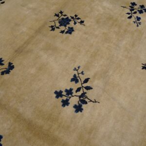 Low-pile beige rug with scattered navy floral designs showing distinct fold creases.