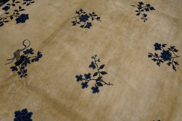 Low-pile beige rug with scattered navy floral designs showing distinct fold creases.