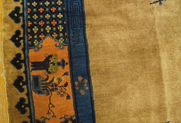 The rug's tan field borders detailed bands of blue, orange, and black floral and geometric patterns.